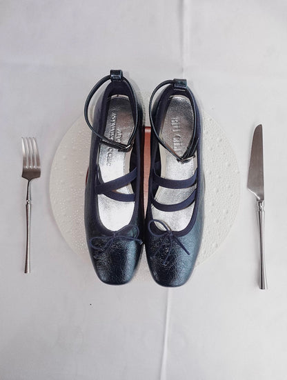 Navy metallic leather Mary Jane ballet flats with asymmetrical cross straps, styled playfully on a white plate with fork and knife as if served at a dinner setting