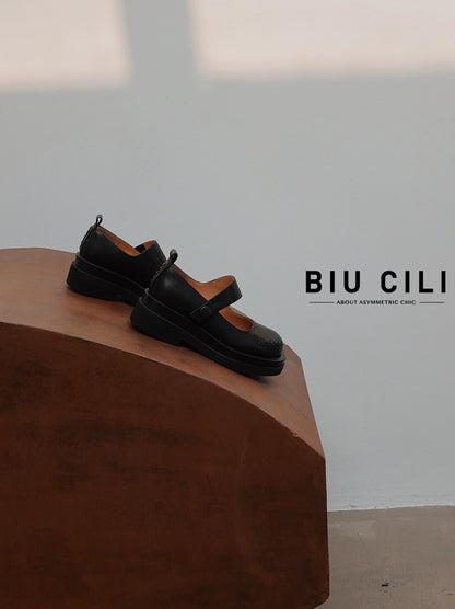 Black platform Mary Jane shoes with wide strap and low block heel, displayed on a wooden surface