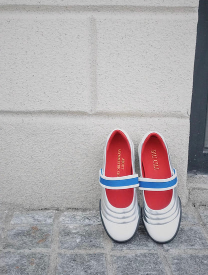 Pair of Kaia leather Mary Jane flats in colorblock white and silver with red lining and blue strap, positioned against a white textured wall