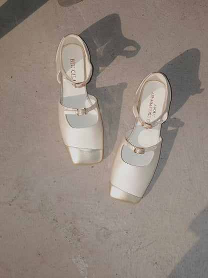 A pair of white silk mary jane flats with straps and asymmetric gold leather details at toe front, placed on the floor
