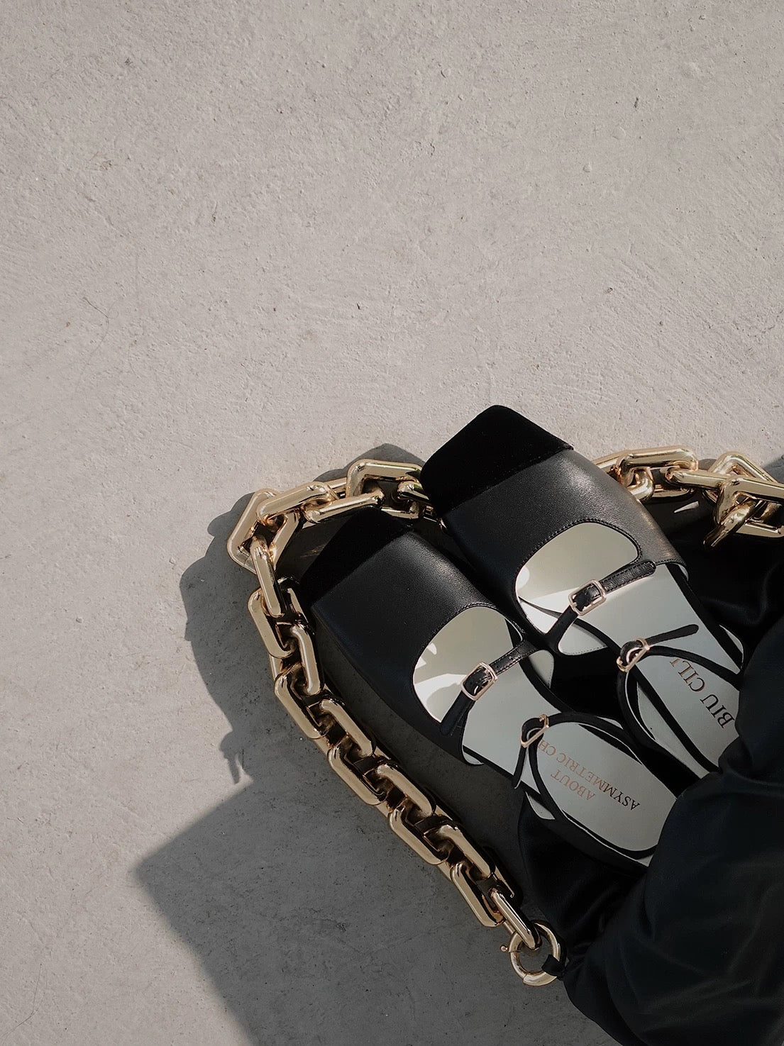 A pair of black leather mary jane flats with straps and asymmetric velvet details at toe front, placed in a backet