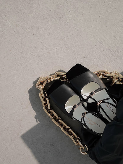A pair of black leather mary jane flats with straps and asymmetric velvet details at toe front, placed in a backet