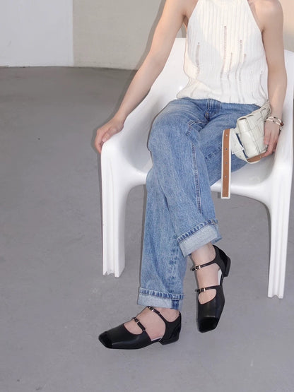 Women wearing a pair of black leather mary jane flats with straps and asymmetric velvet details at toe front, metallic buckles, pairing with jeans and white top, sitting on a white chair