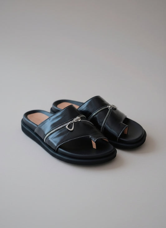 Black sandals with zippers on a wooden surface