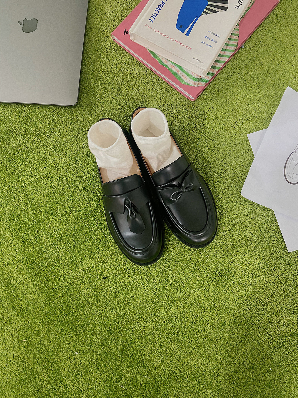 Black leather loafers for women featuring asymmetric tie and bow details, crafted in matte calfskin with low heel and soft structure, place on grass.