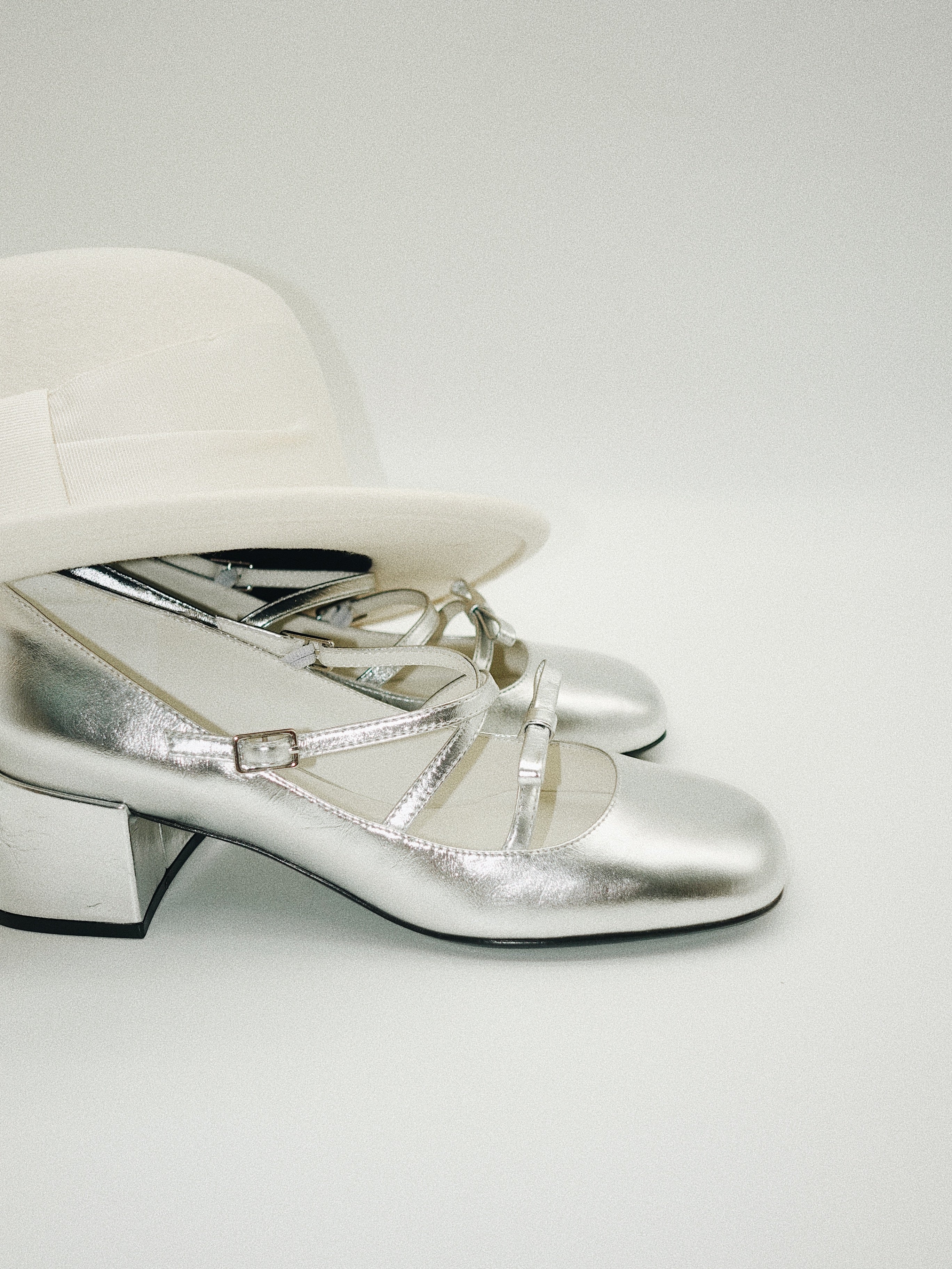 Metallic silver Mary Jane heels with triple asymmetric straps and block heel covered by a hat