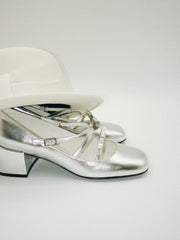 Metallic silver Mary Jane heels with triple asymmetric straps and block heel covered by a hat