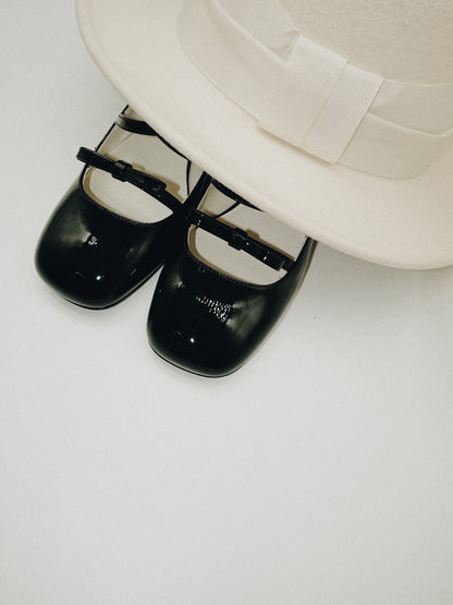 Black patent leather Mary Jane heels with triple straps, block heel, and bow detail.