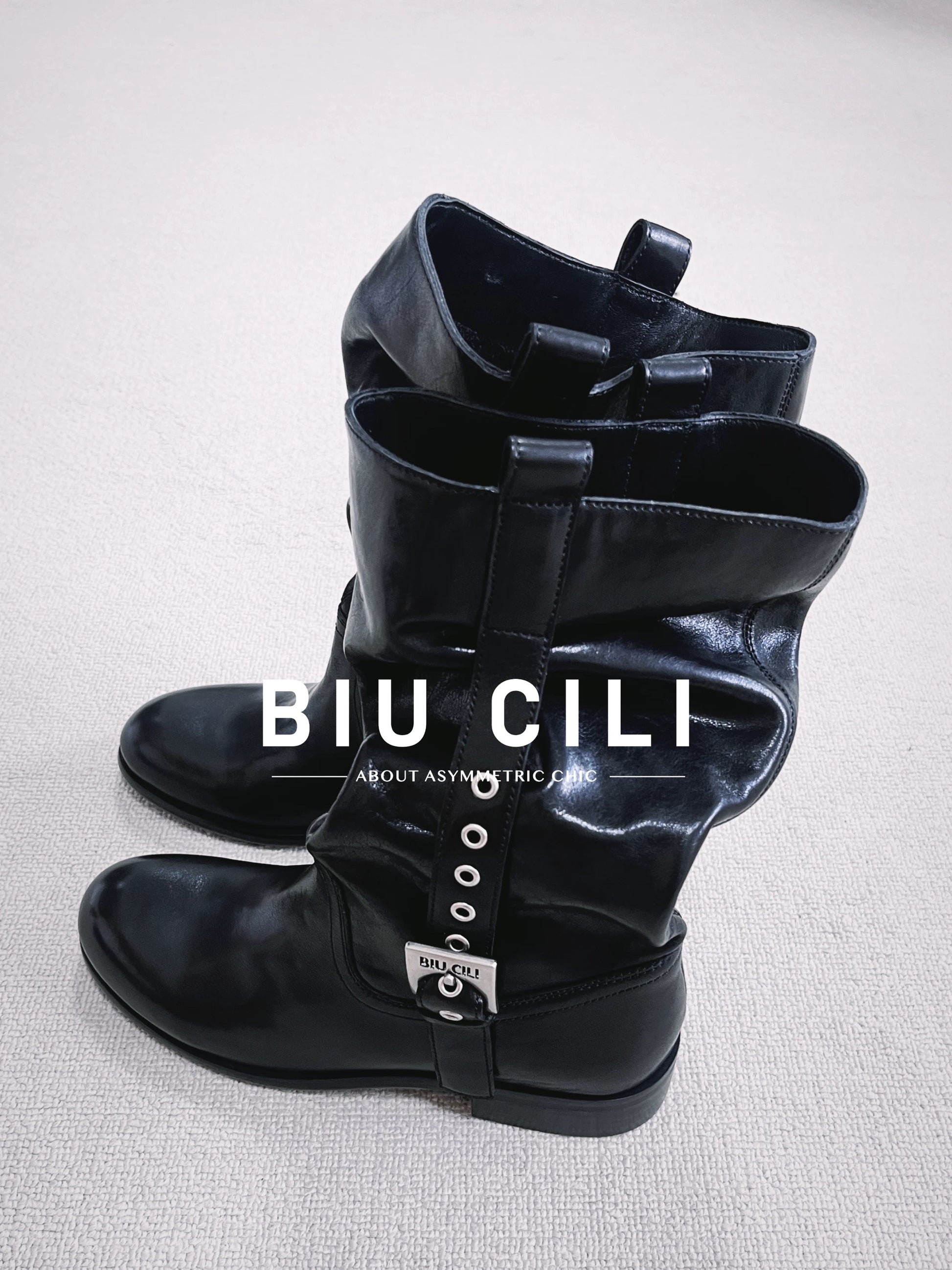 Black low-heeled boots with a strap on a light gray background, featuring the brand 'BIU CILI'.