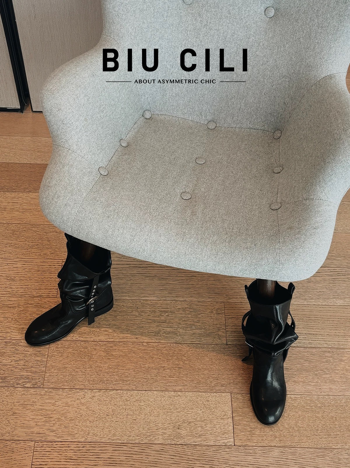 Grey chair wearing pair of slouchy black boots with 'BIU CILI' branding.