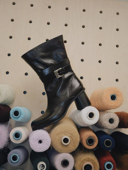 Black leather boot with a buckle on a pegboard with spools of thread.