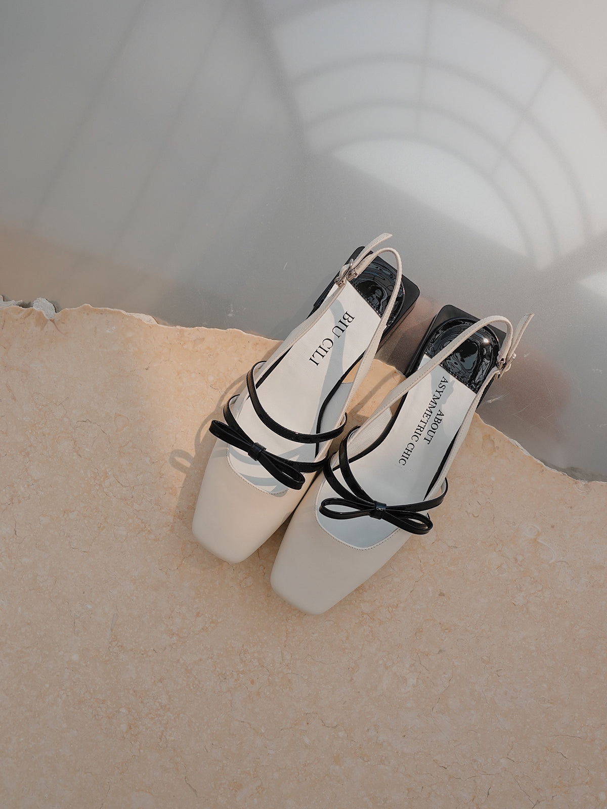 White Mary Jane shoes with square toe and black asymmetric bow straps, contrast heel, and soft leather finish.