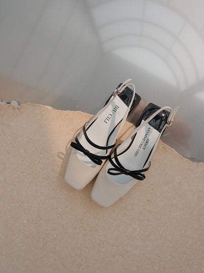 White Mary Jane shoes with square toe and black asymmetric bow straps, contrast heel, and soft leather finish.