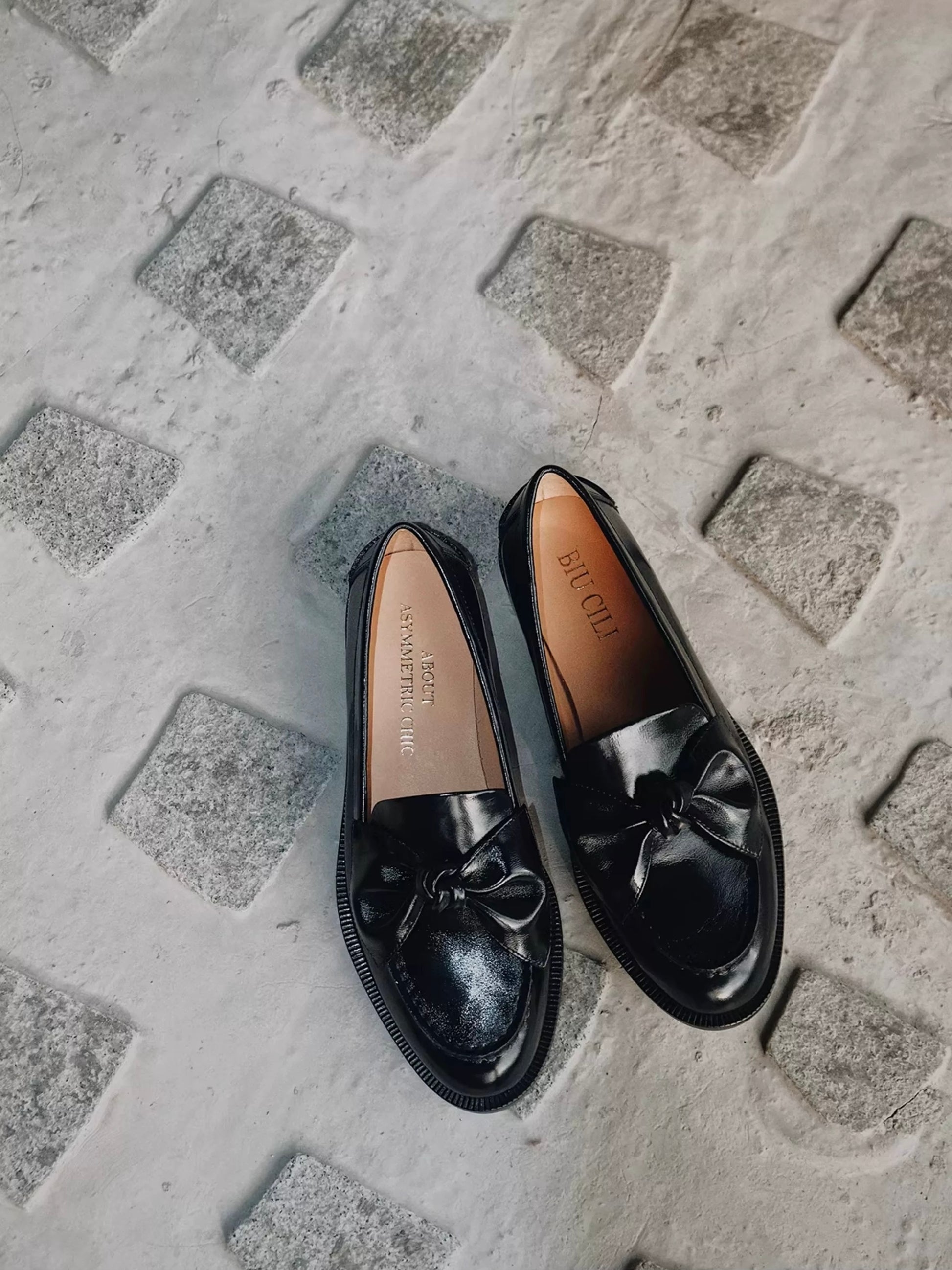 Black loafers with a bow on a textured concrete surface