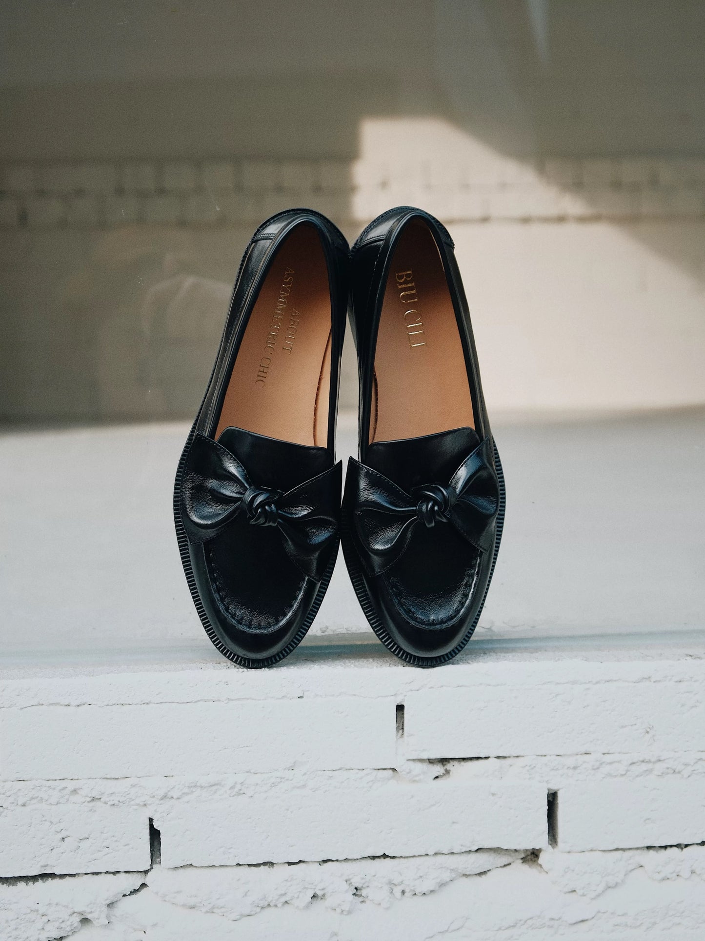 Pair of black loafers with bow details on a white wooden floor.