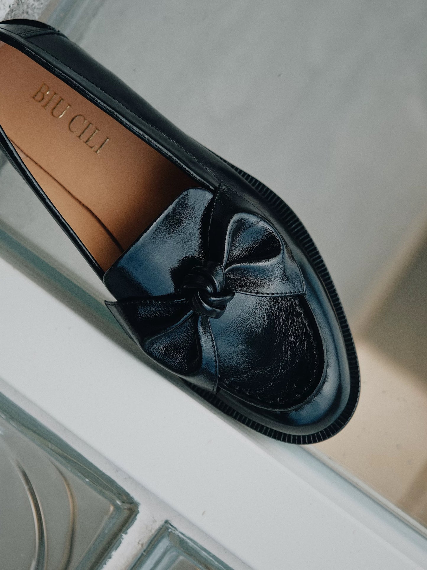 Black loafer shoe with a bow detail on a neutral background