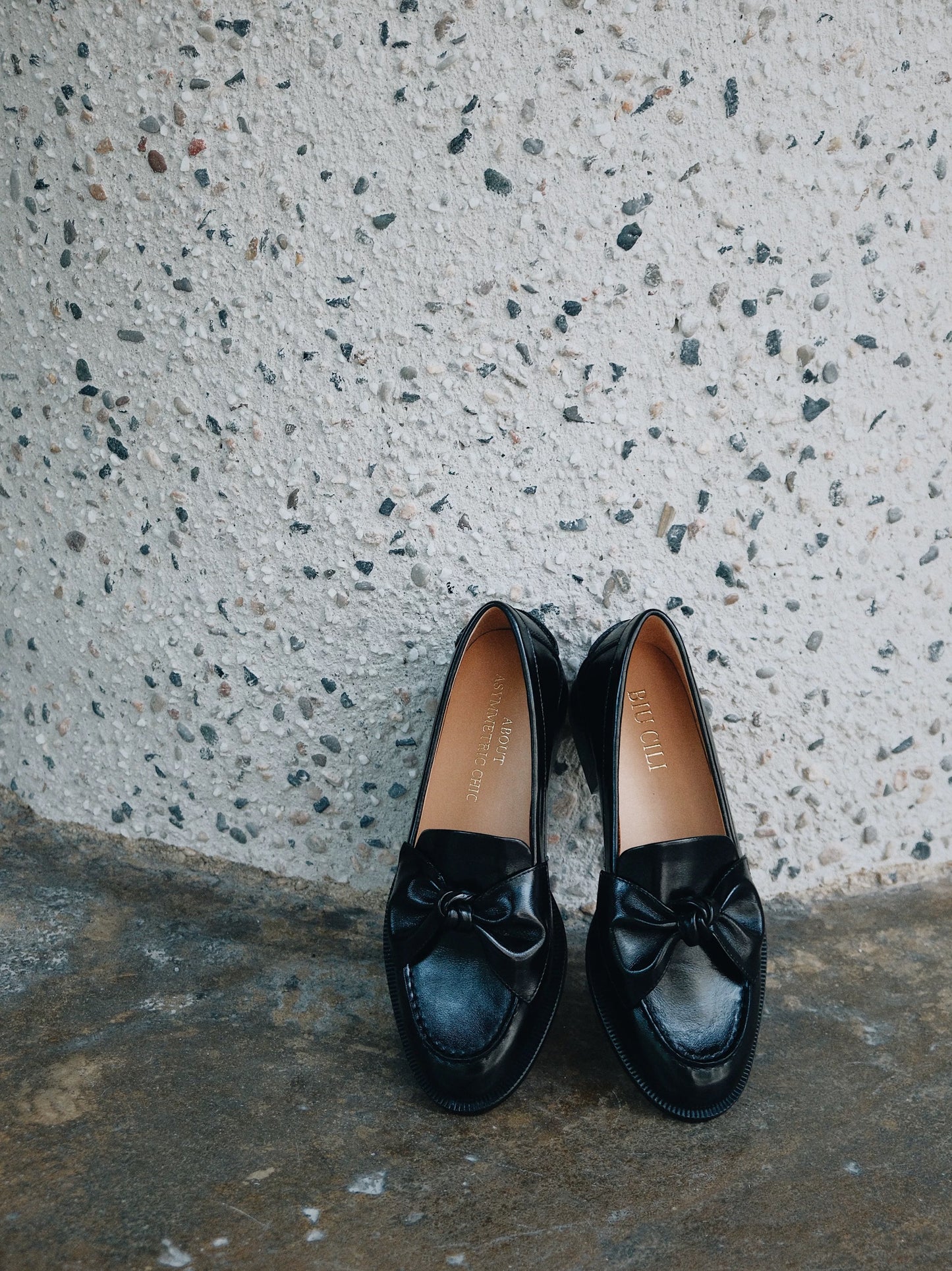 Pair of black loafers with bows on a textured concrete surface