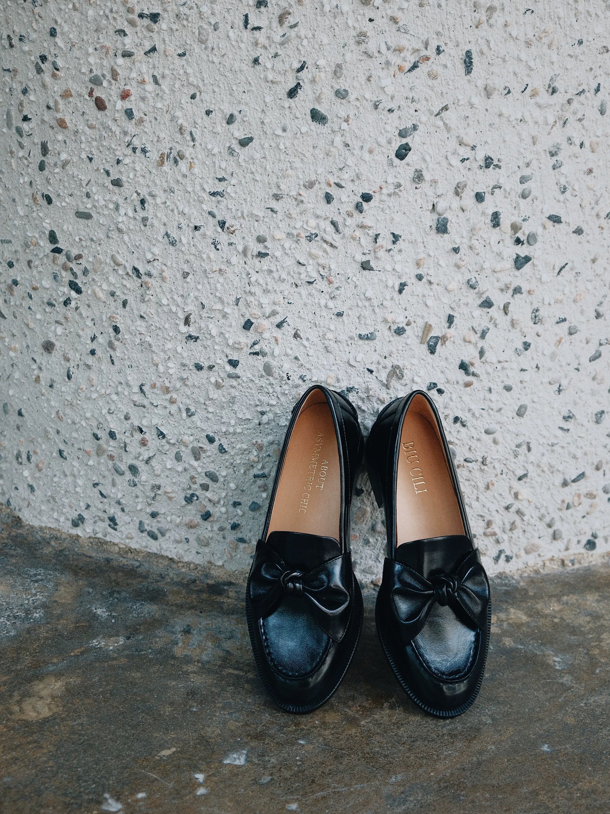 Pair of black loafers with bows on a textured concrete surface