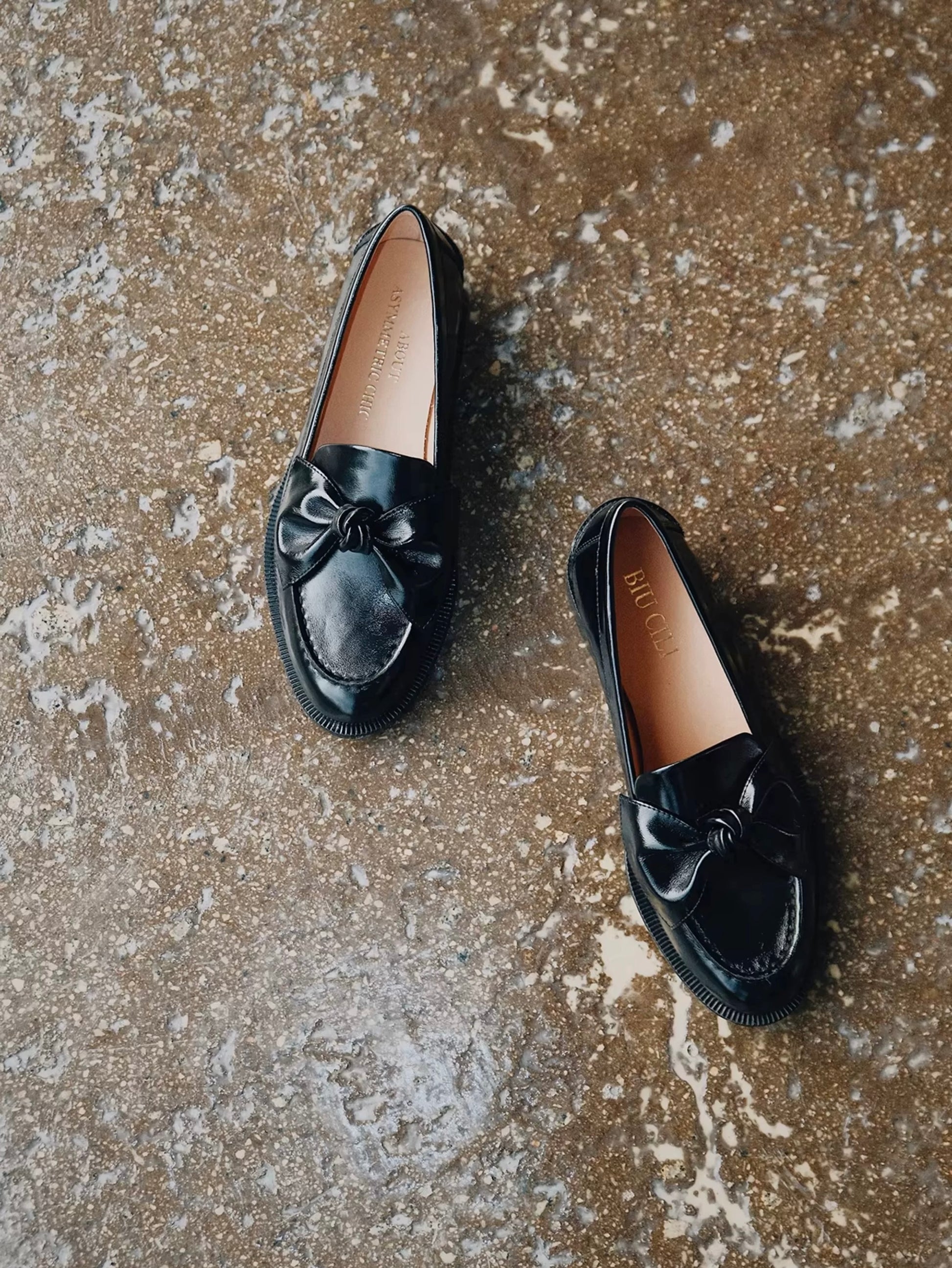 Pair of black loafers with bow details on a textured brown surface