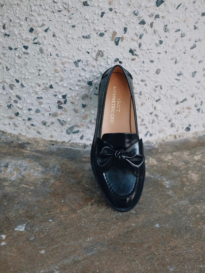 Black loafer shoe with a bow on a textured concrete surface