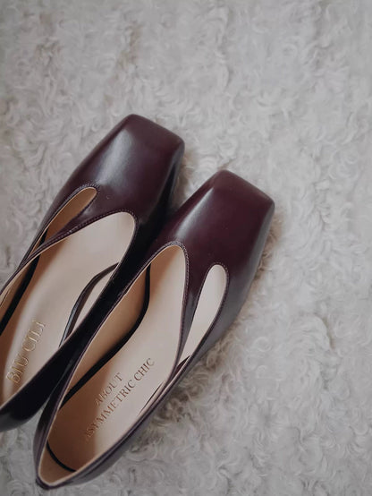 Pair of maroon high heels with white soles on a textured surface