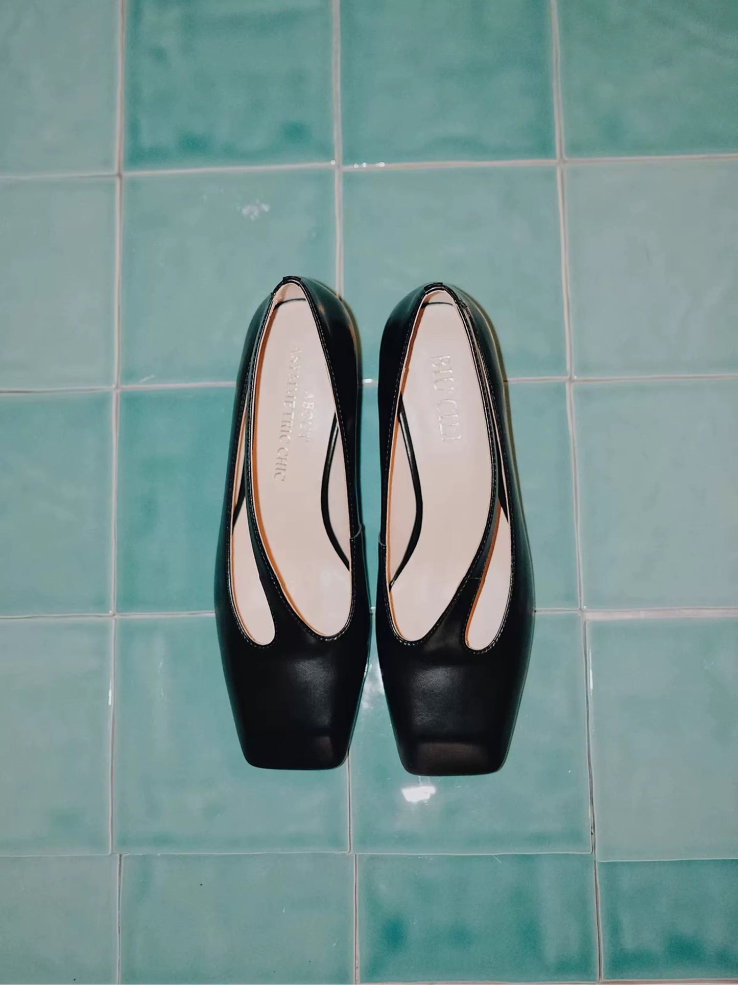 Black high-heeled shoes on a green tiled floor