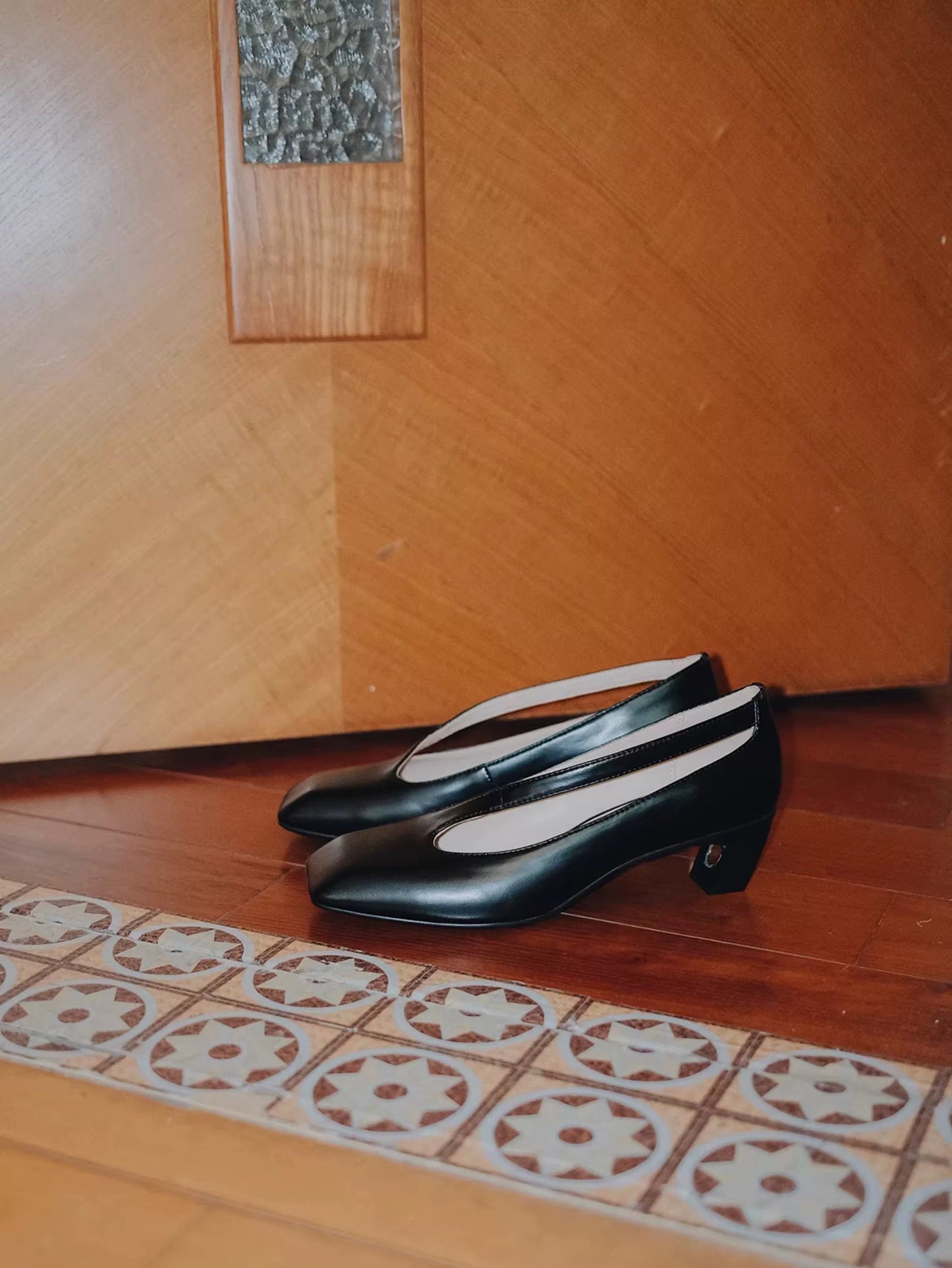 Pair of black shoes on a wooden floor with a decorative rug.