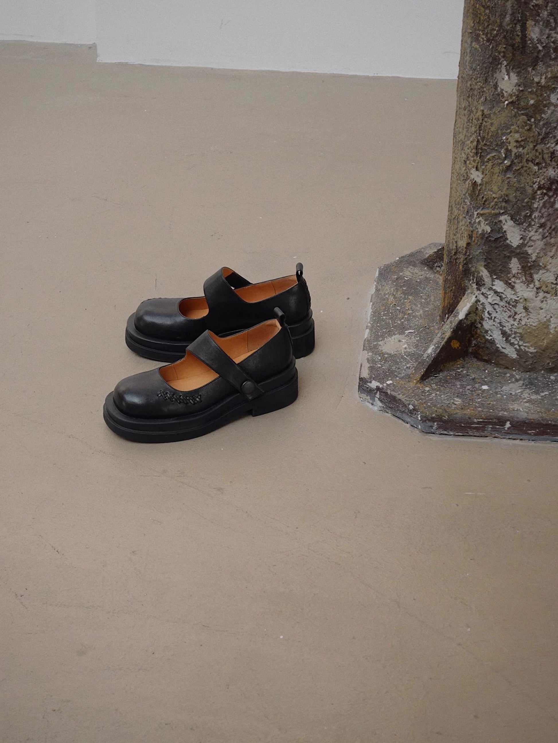 Black platform Mary Jane shoes with wide strap and low block heel, displayed on a textured concrete floor