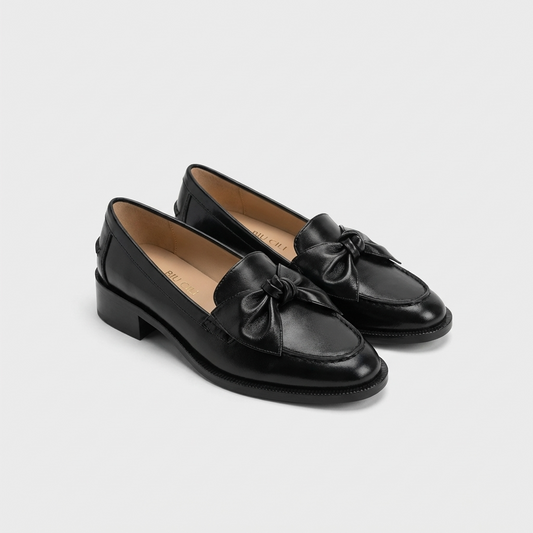 Pair of black loafers with bow details on a light gray background